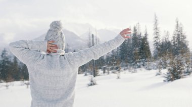 Genç bir kadın kar yağışı yapıyor ve ellerini dağa kaldırıyor.