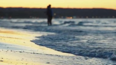 Arka planda akşam gökyüzüne karşı dalgaların olduğu bir plajın kıyısında.