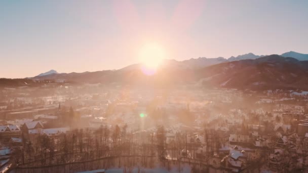Солнце светит за горами против города с небольшими домами на переднем плане — стоковое видео