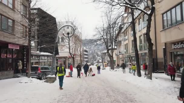 Les gens marchent sur une rue enneigée avec des branches d'arbres couvertes de neige — Video