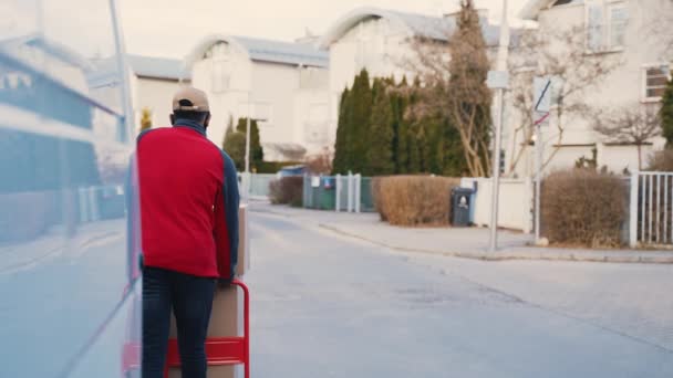 Man med ansiktsmask driver vagn med pappkartonger. Leverans av varor under en pandemi — Stockvideo