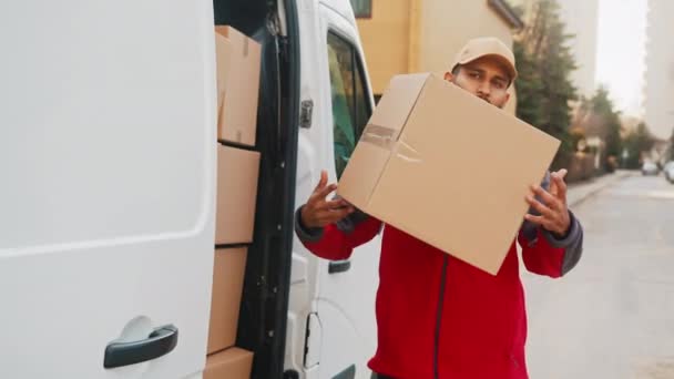 Молодой человек выгружает картонные коробки из грузовика — стоковое видео
