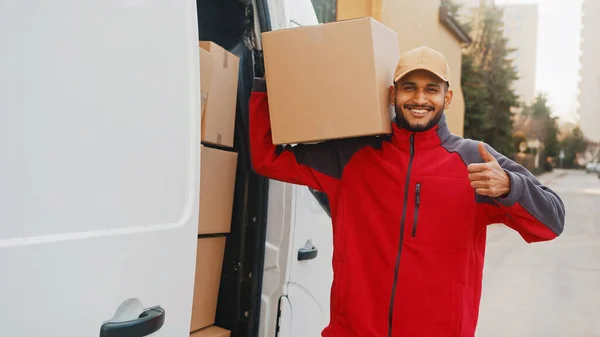 Smiling delivery man showing thumb up and looking at camera