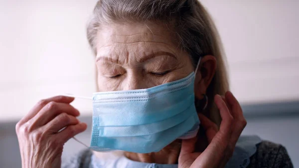 Пожилая одинокая женщина надевает медицинскую маску на лицо — стоковое фото