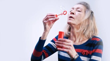 Parti şapkalı yaşlı kadın sabun köpüğü üflüyor.