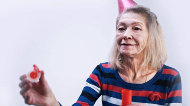 Parti şapkalı yaşlı kadın sabun köpüğü üflüyor.