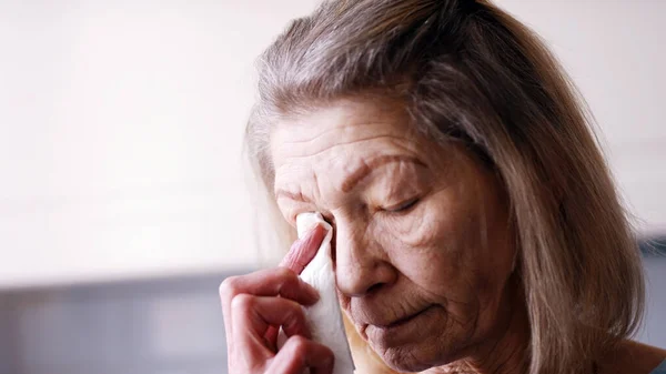 Deprimida velha mulher solitária enxugando lágrimas com tecido enquanto olhava pela janela — Fotografia de Stock