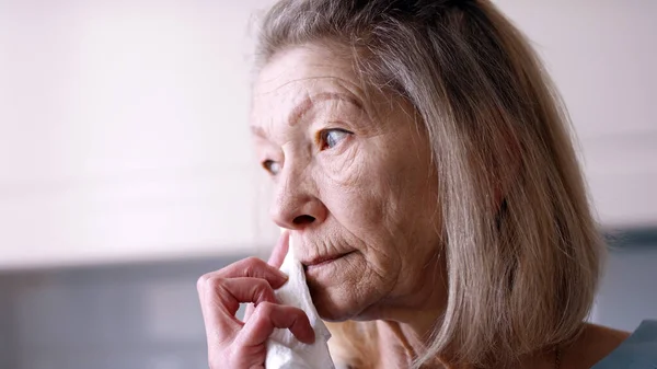 Пожилая женщина вытирает рот салфеткой, глядя в окно — стоковое фото