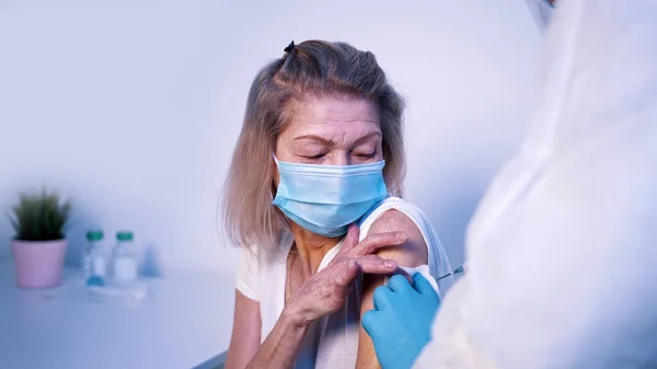 Doctor dándole la vacuna Covid a una mujer mayor con mascarilla facial. Vacunación e inmunización durante el coronavirus — Foto de Stock