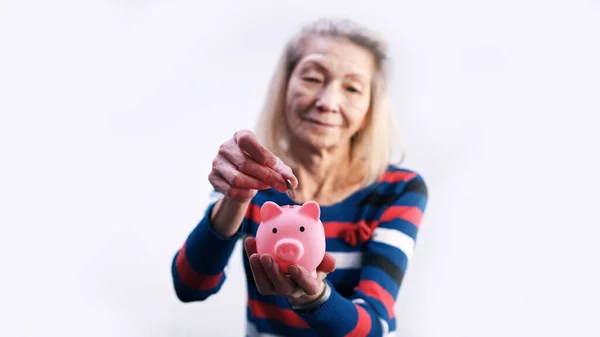 Starsza emerytka wkładająca monety do skarbonki. Skupienie selektywne — Zdjęcie stockowe