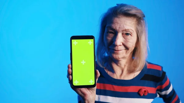Stará žena se široce otevřenýma očima drží smartphone se zelenou obrazovkou — Stock fotografie