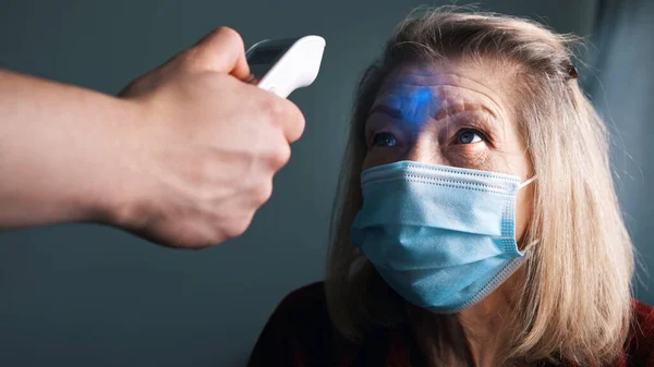 Termómetro digital que mide la temperatura corporal de una anciana con máscara médica — Foto de Stock