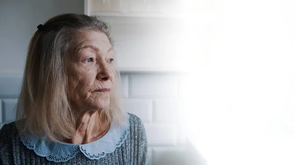 Traurige alte grauhaarige Frau, die aus dem Fenster schaut. Verletzliche Person in Quarantäne — Stockfoto