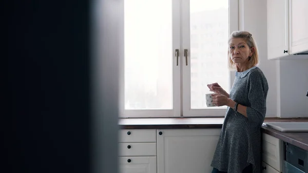 Lonely mulher idosa bebendo café de pé em sua cozinha — Fotografia de Stock