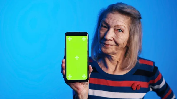 Mujer de edad con los ojos bien abiertos sosteniendo teléfono inteligente con pantalla verde — Foto de Stock