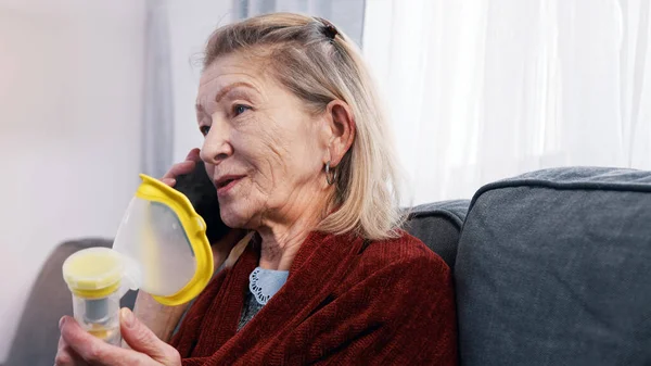 Ηλικιωμένη γυναίκα που χρησιμοποιεί εισπνευστήρα οξυγόνου ενώ της τηλεφωνούν. Ευάλωτο άτομο κατά τη διάρκεια επιδημίας κοπριάς — Φωτογραφία Αρχείου