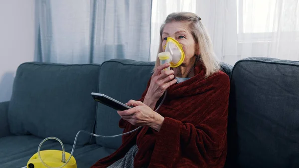 Mujer anciana usando máscara de oxígeno mientras cambia canales en la televisión en casa — Foto de Stock