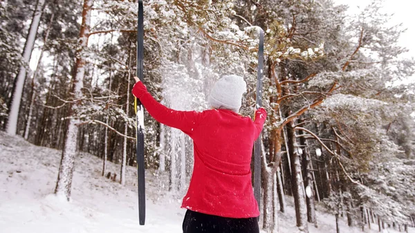 Kobieta trzymająca narty w rozciągniętych dłoniach przed zimowym lasem — Zdjęcie stockowe