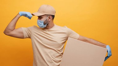 Yüzü maskeli güçlü genç kurye. Karton kutuyu bükerken kaslarını kasıyor.