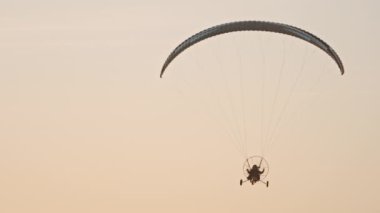 Paramotor gün batımına karşı kameradan uçuyor.