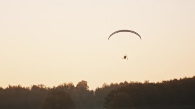 Paramotor silueti ağaçların üzerinde uçuyor.