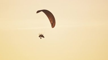 Paramotor silueti gün batımına karşı havada uçuyor.