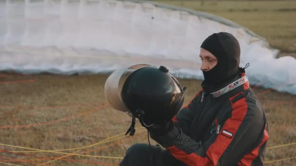 Hombre sentado en la hierba poniéndose casco de seguridad con parabrisas — Vídeos de Stock