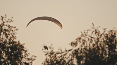 Paramotor gün batımına karşı havada uçuyor.