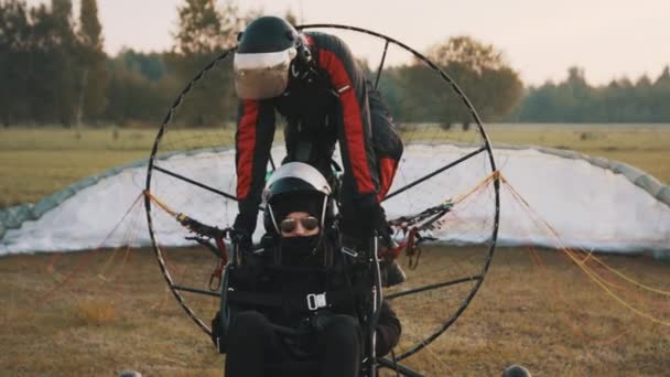 Pilot getting on paramotor trike on seat between client and propeller — Stock Video