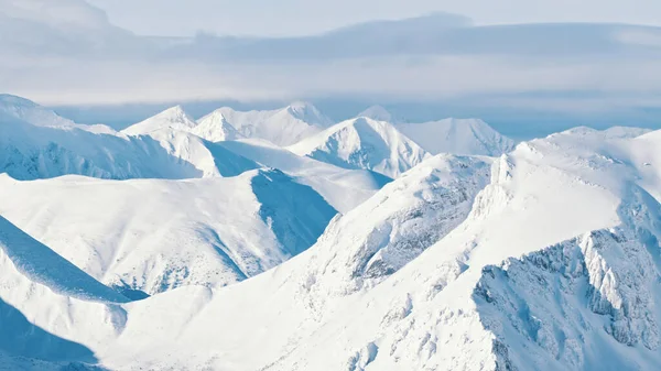 Śnieżne szczyty górskie z zachmurzonym błękitnym niebem w tle - Góry Zimowe — Zdjęcie stockowe