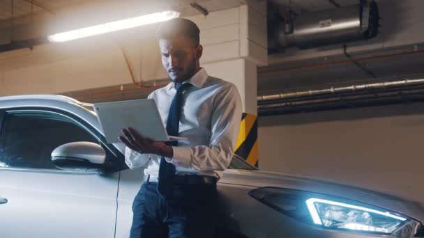 Homem sorridente feliz apoiando-se em carro de prata. Empresário bem sucedido segurando computador portátil e olhando para longe. — Vídeo de Stock