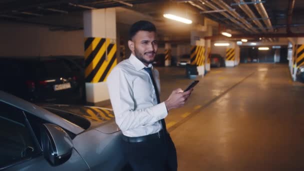 Un homme d'affaires souriant fait un appel vidéo dans un garage souterrain — Video