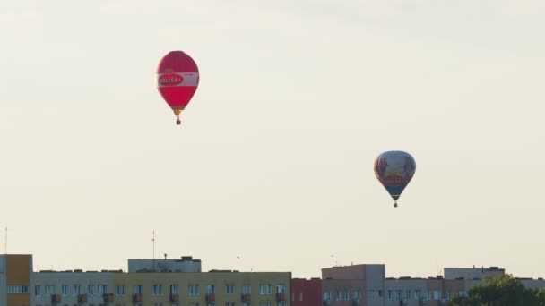 Два красочных воздушных шара над жилыми квартирами против чистого белого неба — стоковое видео