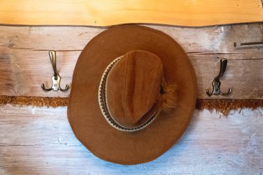 Üzerinde kahverengi şapkası asılı bir duvar askısı. Metal kancalı ahşap duvar askısı