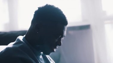 Evdeki kanepede dizüstü bilgisayarını kullanan Afro-Amerikalı bir adam.