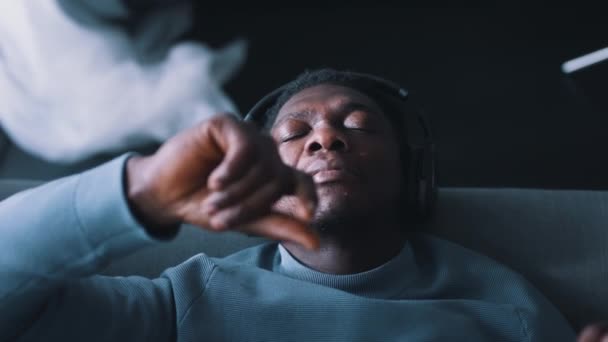 Uomo afroamericano con le cuffie che ascolta musica sdraiato sul divano — Video Stock