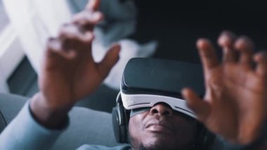 Sanal gerçeklik gözlüğü ve kulaklık takan Afro-Amerikalı bir adam kanepede yatıyordu.