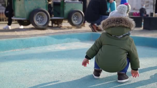 Arka planda, dışarıda çocuk parkında kürklü kapüşonlu ceket giyen bir çocuk var. — Stok video