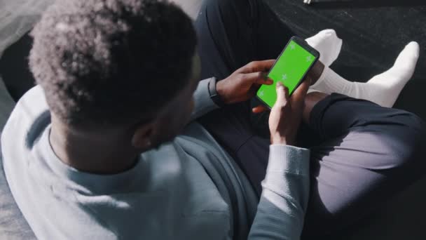 Kanepede bağdaş kurup cep telefonunu kullanan bir adamın yüksek açılı görüntüsü. — Stok video