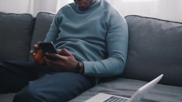 Muž sedící na gauči ve sluchátkách pomocí mobilu — Stock video
