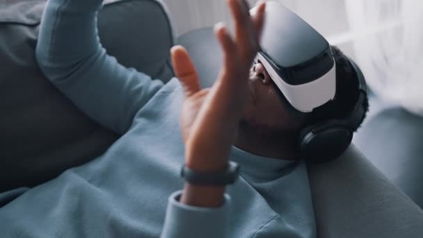 Афроамериканець, одягнений у віртуальні окуляри та навушники, лежить на Парі — стокове відео
