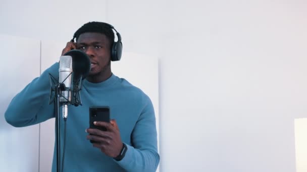 Человек в наушниках поет песню в микрофон в студии — стоковое видео