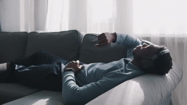 Hombre afroamericano con auriculares escuchando música - Lying On The Couch — Vídeo de stock