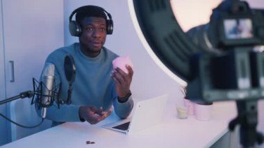 Kulaklık takan ve elinde kumbarayla video kaydeden bir adam. 