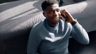  Afro-Amerikalı bir adam yerde oturmuş telefonuyla birileriyle konuşuyor.