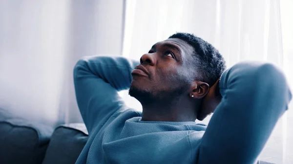 Serious man thinking while sitting on a blue sofa - Hands behind the head