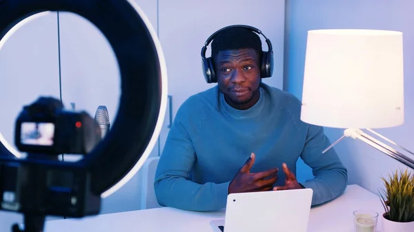 Afro-Amerikaanse man met een koptelefoon aan tafel die iets uitlegt. Concept van online klassen of podcasts. Opname in de studio. — Stockfoto