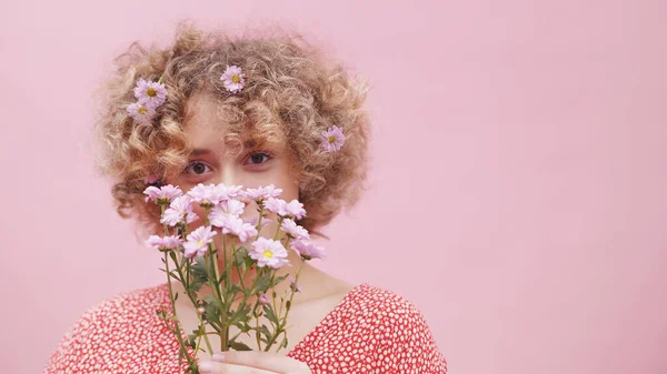 Schöne junge kaukasische Frau mit einem Strauß Frühlingsblumen über ihrem Gesicht und Blumenschmuck in ihrem lockigen Haar lächelnd. Nahaufnahme — Stockfoto