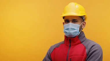 Kolları çaprazlanmış, güvenlik kaskı ve maske takan Hintli mühendis.