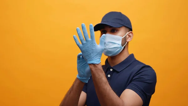 El repartidor se pone los guantes. El uso de una máscara y una gorra azul - Covid 19 — Foto de Stock